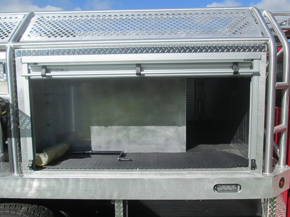 Exterior view of small fire truck showing cab, body compartments, and wheel/tire area.