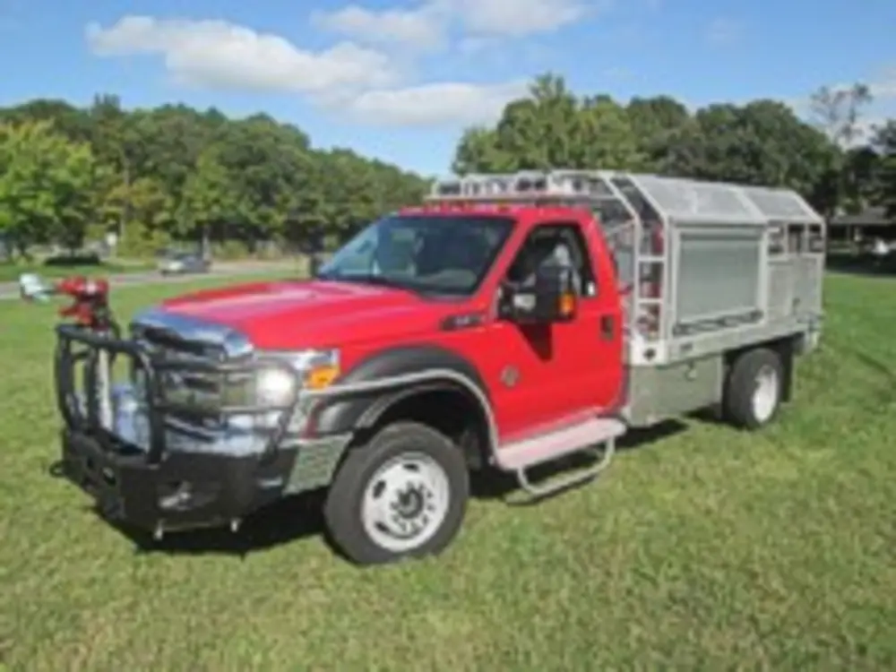 Exterior view of small fire truck showing cab, body compartments, and wheel/tire area.