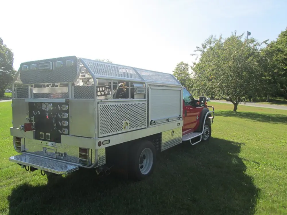 Exterior view of small fire truck showing cab, body compartments, and wheel/tire area.