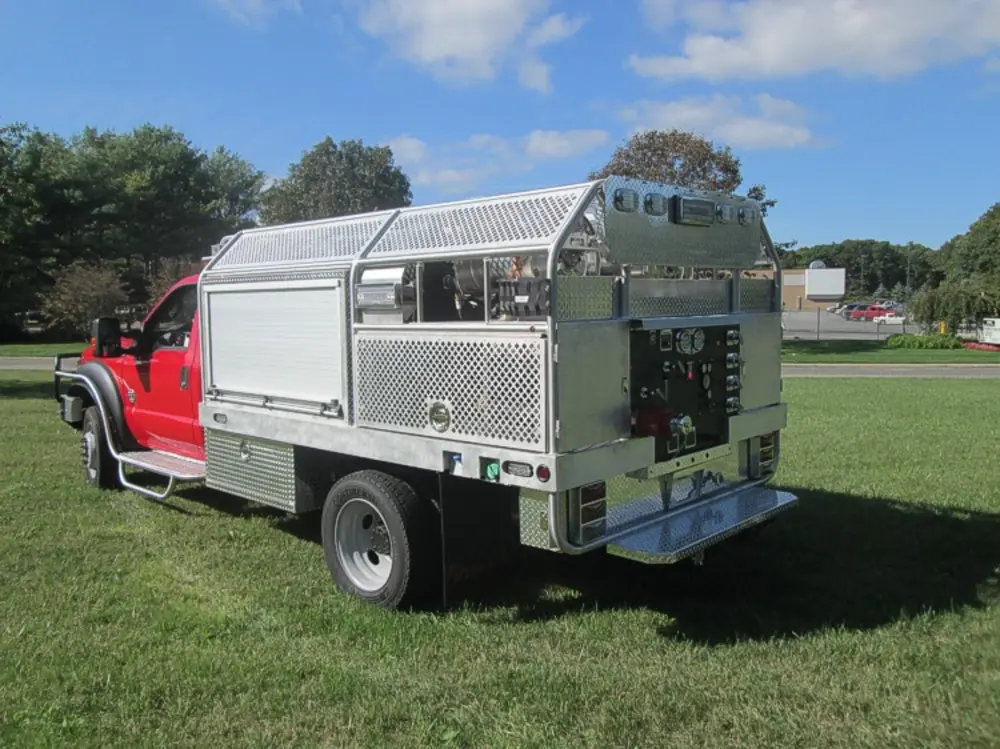 Exterior view of small fire truck showing cab, body compartments, and wheel/tire area.