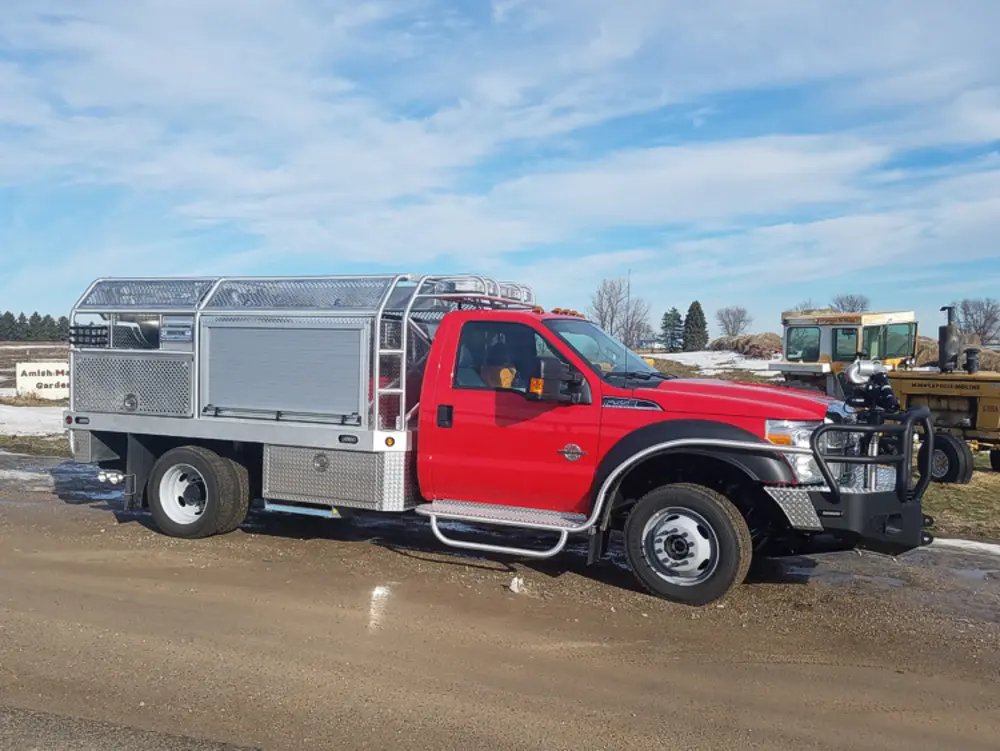 Exterior view of small fire truck showing cab, body compartments, and wheel/tire area.