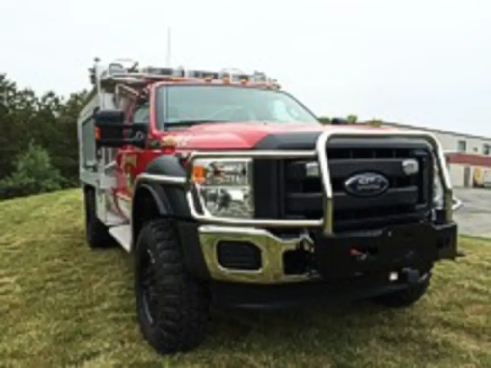 Exterior view of small fire truck showing cab, body compartments, and wheel/tire area.