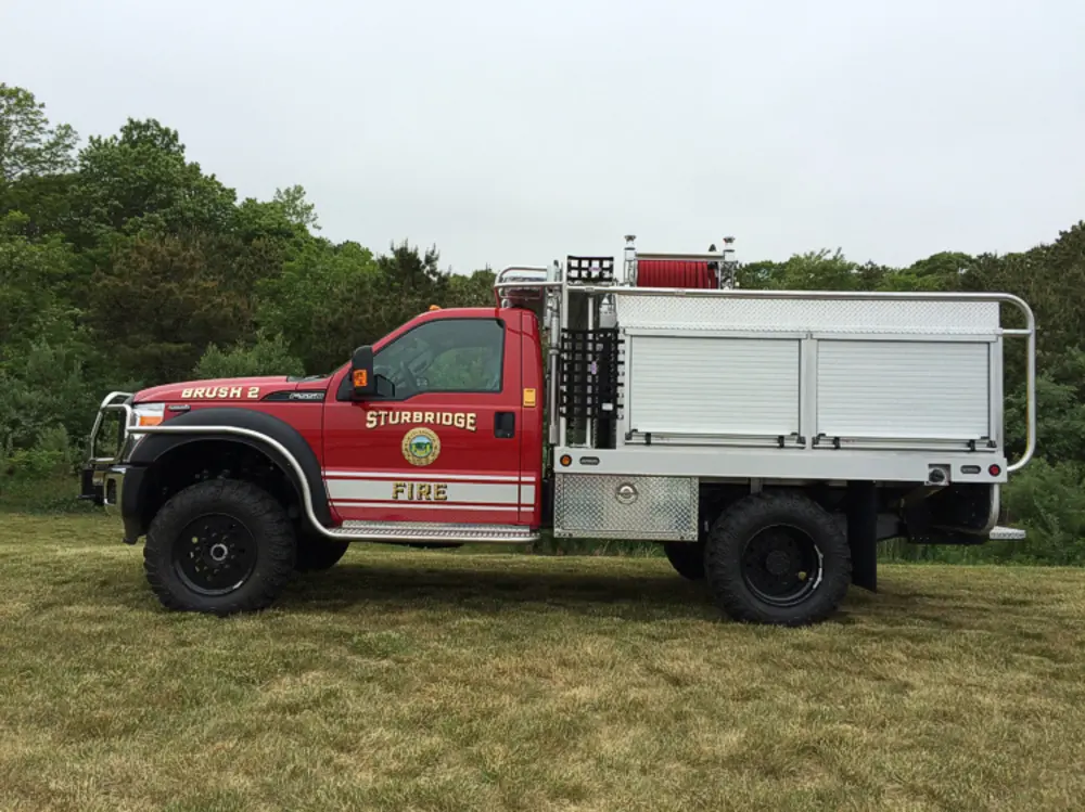 Exterior view of small fire truck showing cab, body compartments, and wheel/tire area.