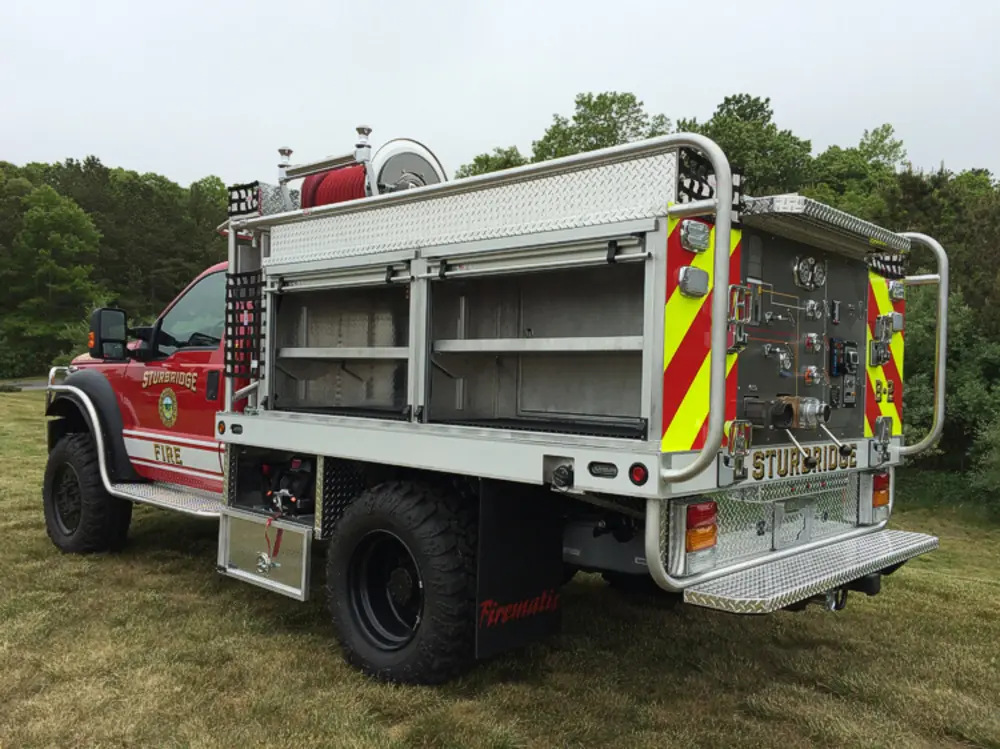 Exterior view of small fire truck showing cab, body compartments, and wheel/tire area.