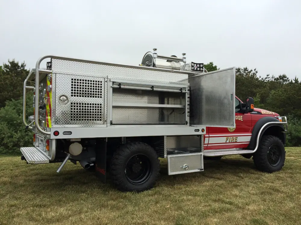 Exterior view of small fire truck showing cab, body compartments, and wheel/tire area.