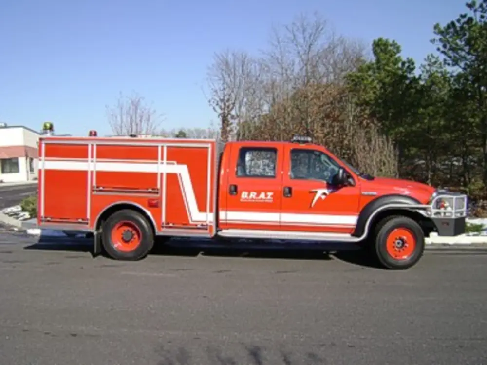 Exterior view of small fire truck showing cab, body compartments, and wheel/tire area.