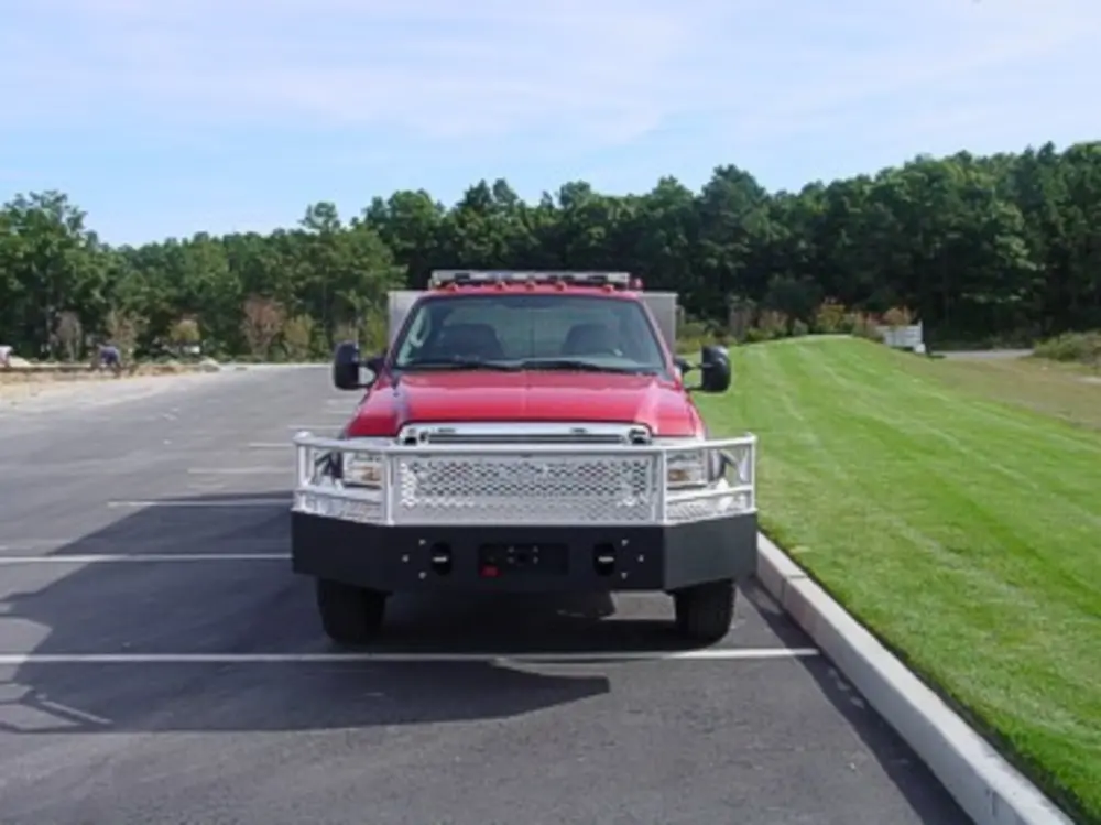 Exterior view of small fire truck showing cab, body compartments, and wheel/tire area.