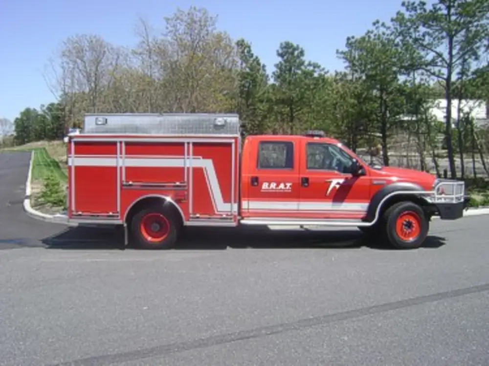 Exterior view of small fire truck showing cab, body compartments, and wheel/tire area.