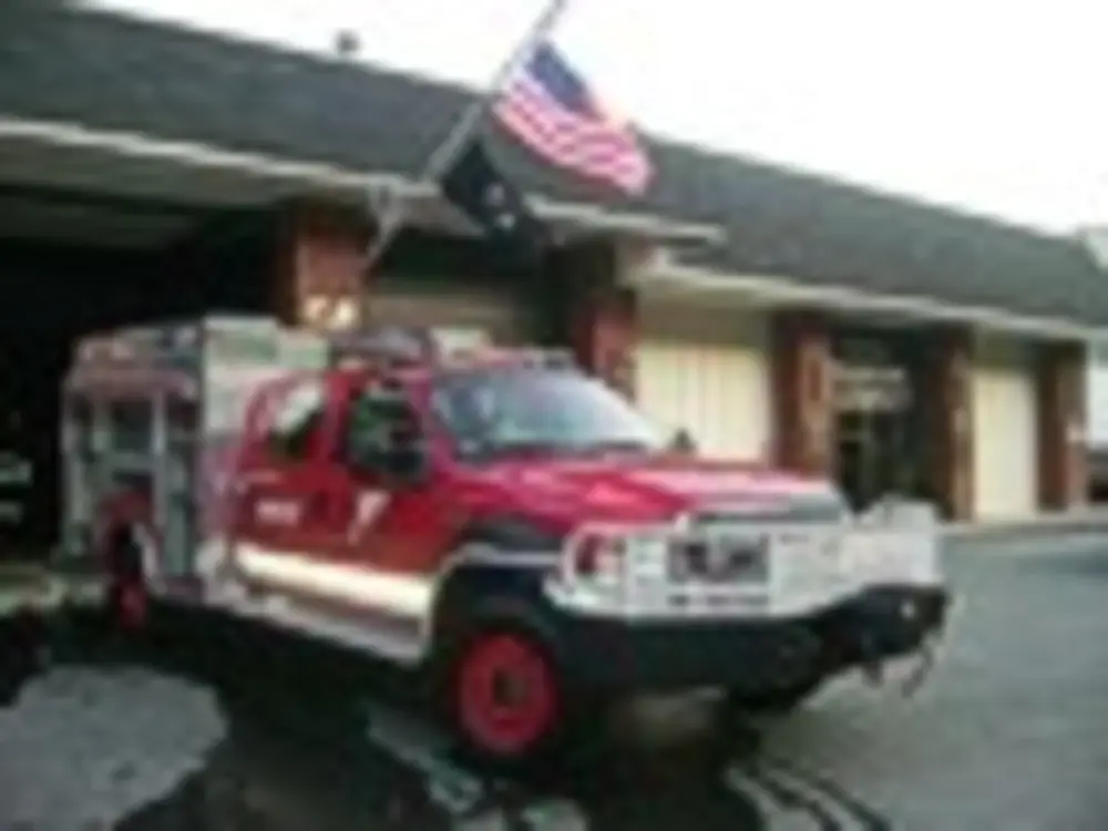 Exterior view of small fire truck showing cab, body compartments, and wheel/tire area.