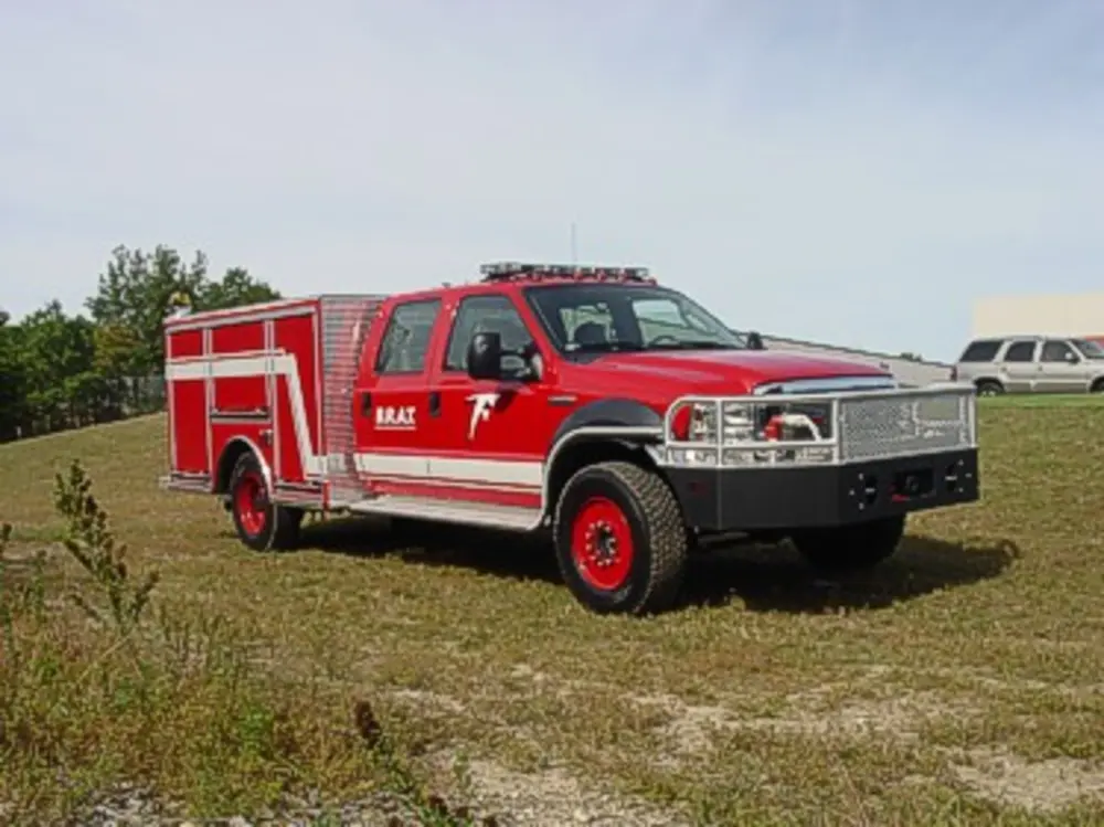 Exterior view of small fire truck showing cab, body compartments, and wheel/tire area.