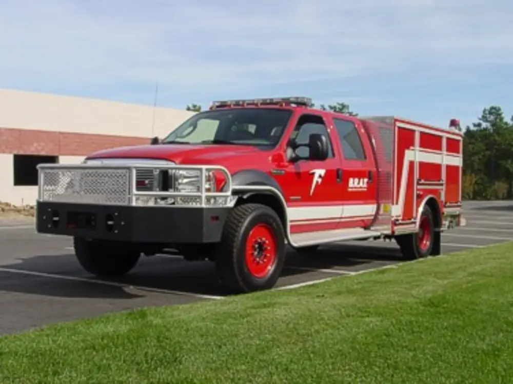 Exterior view of small fire truck showing cab, body compartments, and wheel/tire area.