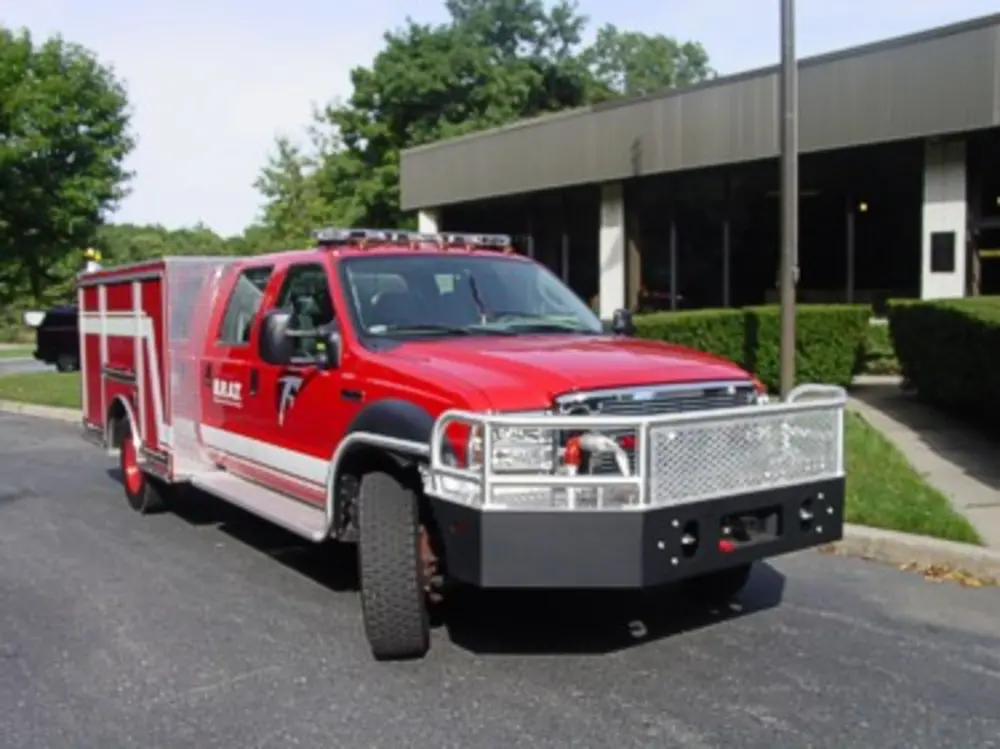 Exterior view of small fire truck showing cab, body compartments, and wheel/tire area.