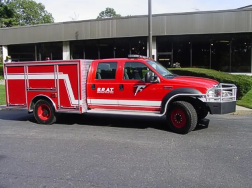 Exterior view of small fire truck showing cab, body compartments, and wheel/tire area.