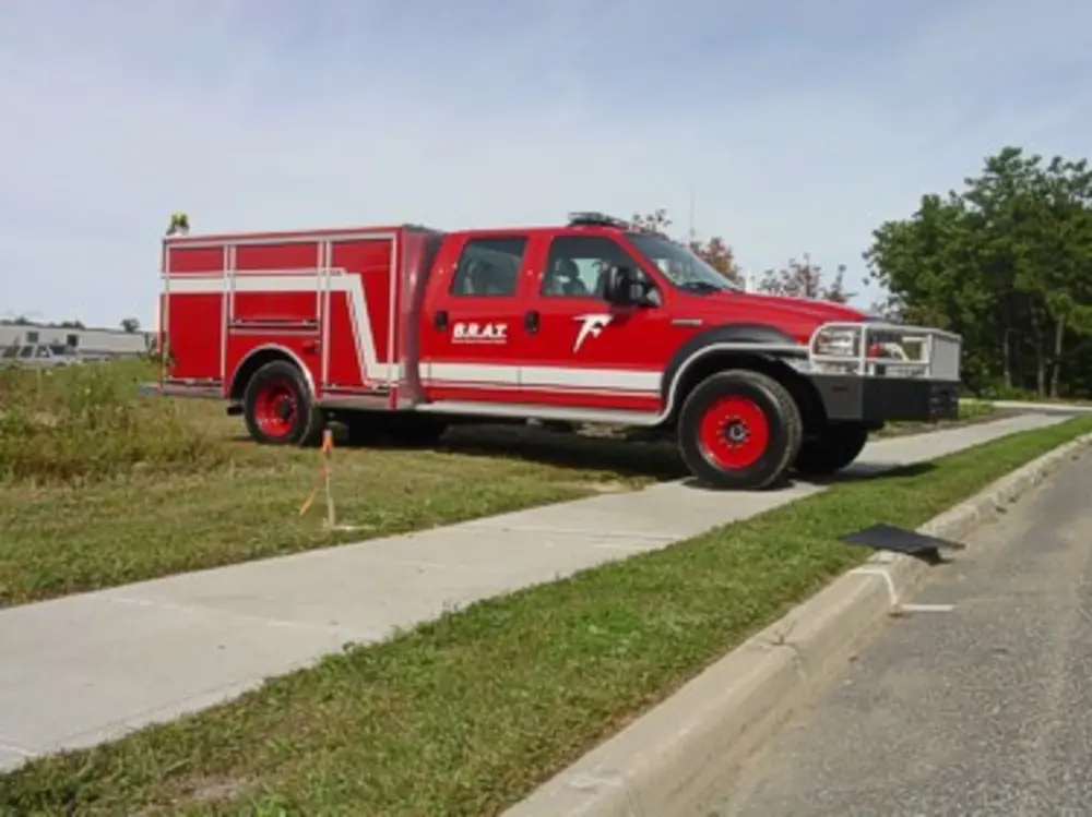 Exterior view of small fire truck showing cab, body compartments, and wheel/tire area.