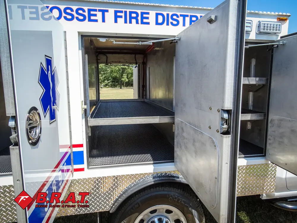 Exterior view of small fire truck showing cab, body compartments, and wheel/tire area.