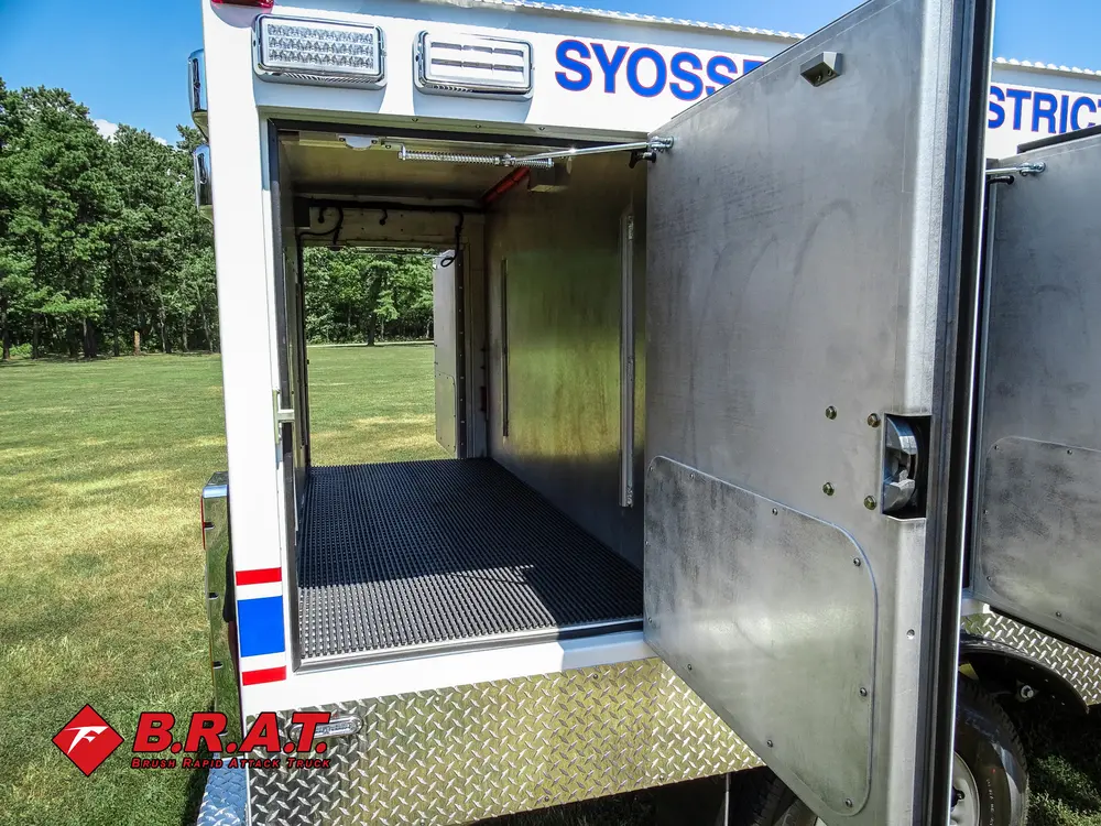 Exterior view of small fire truck showing cab, body compartments, and wheel/tire area.