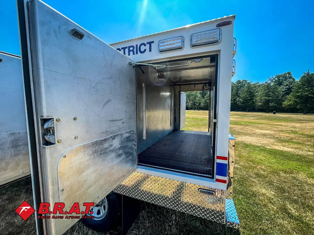 Exterior view of small fire truck showing cab, body compartments, and wheel/tire area.