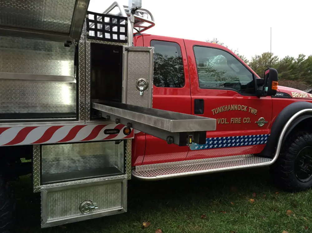 Exterior view of small fire truck showing cab, body compartments, and wheel/tire area.