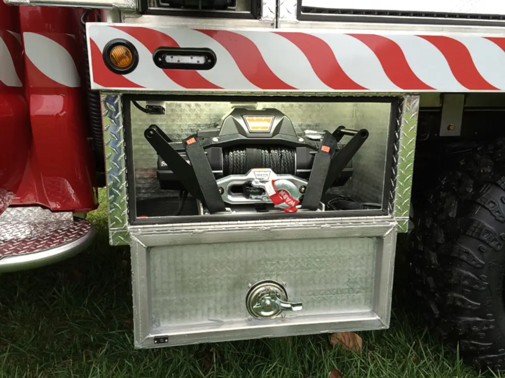 Exterior view of small fire truck showing cab, body compartments, and wheel/tire area.