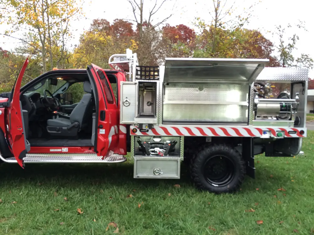 Exterior view of small fire truck showing cab, body compartments, and wheel/tire area.