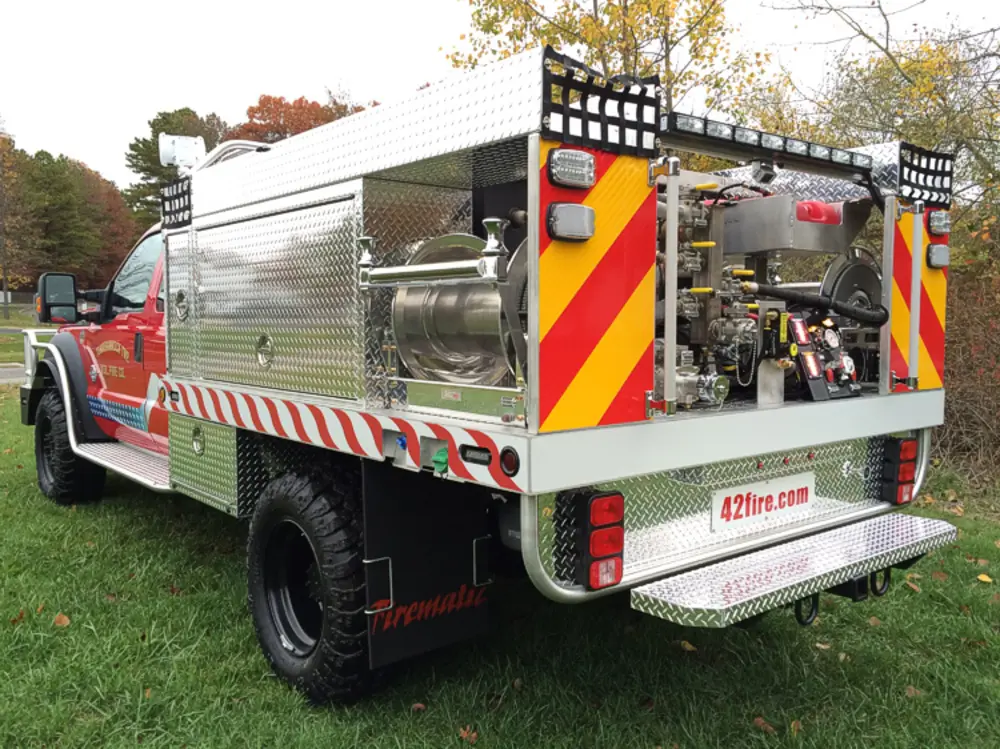 Exterior view of small fire truck showing cab, body compartments, and wheel/tire area.