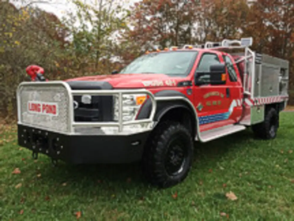 Exterior view of small fire truck showing cab, body compartments, and wheel/tire area.