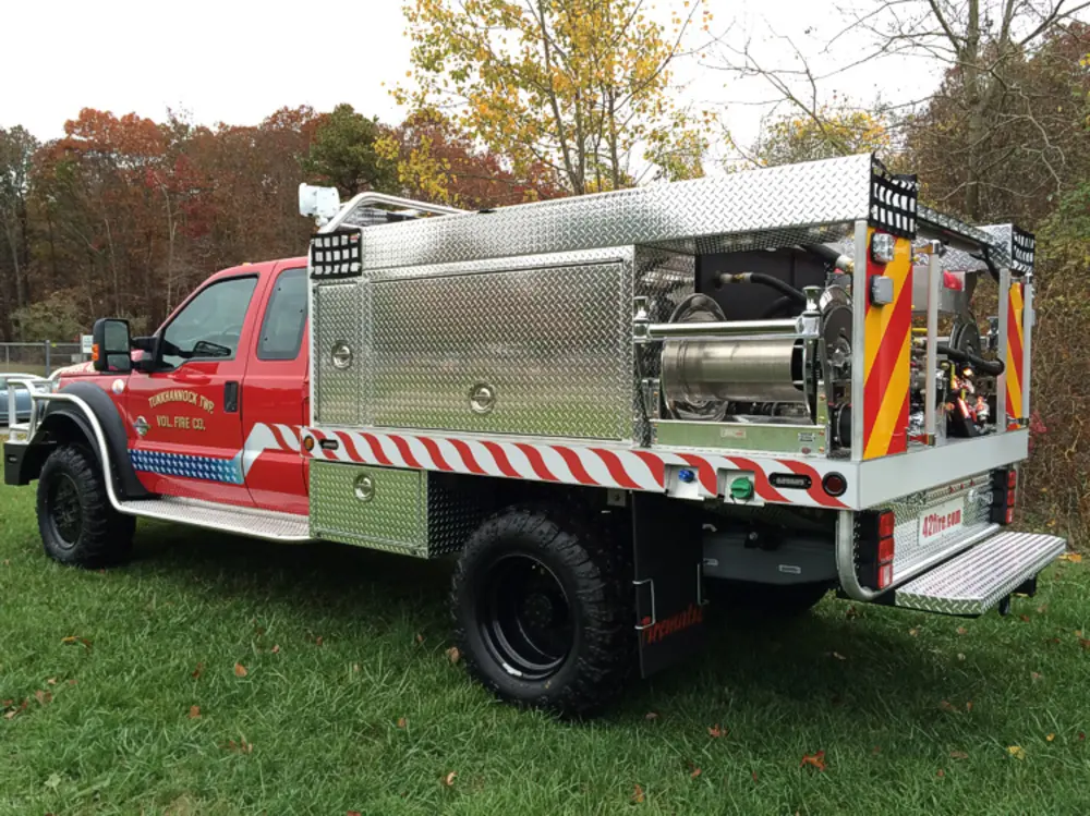 Exterior view of small fire truck showing cab, body compartments, and wheel/tire area.