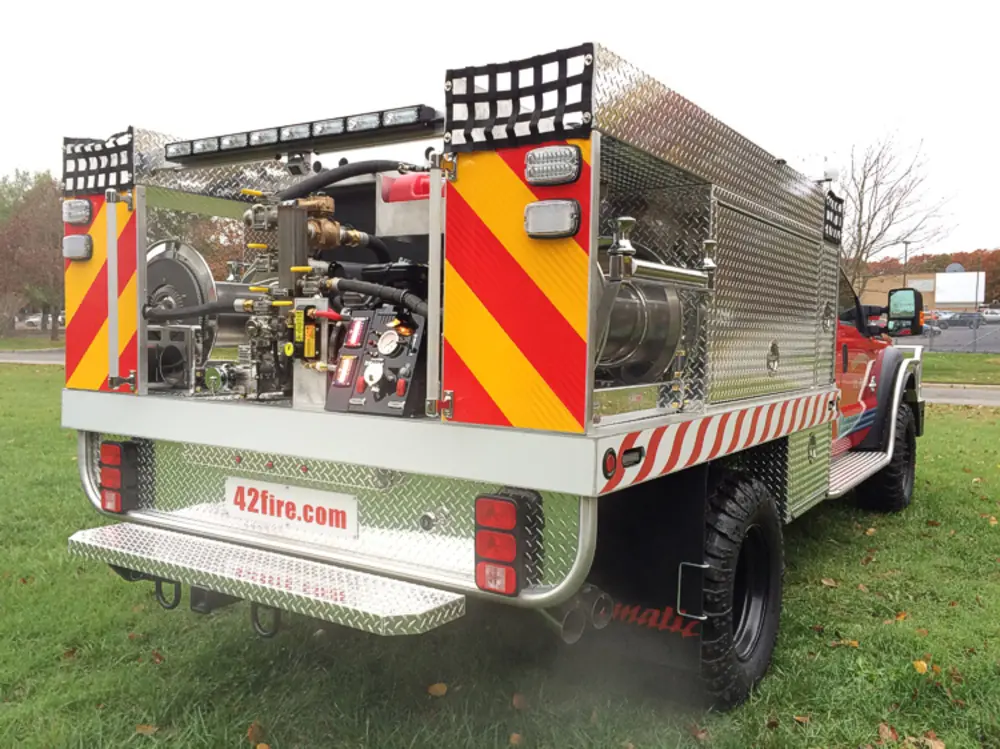 Exterior view of small fire truck showing cab, body compartments, and wheel/tire area.