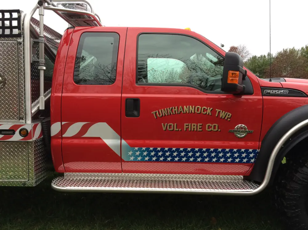 Exterior view of small fire truck showing cab, body compartments, and wheel/tire area.