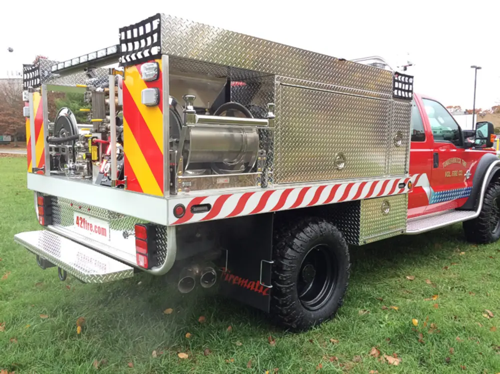 Exterior view of small fire truck showing cab, body compartments, and wheel/tire area.