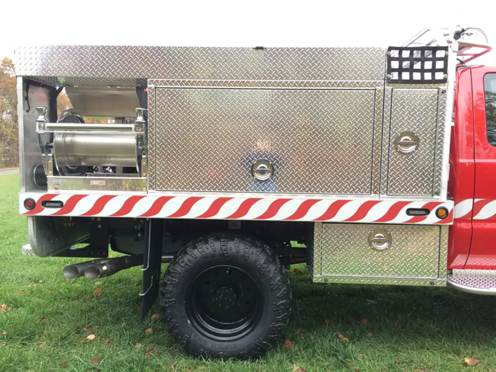 Exterior view of small fire truck showing cab, body compartments, and wheel/tire area.