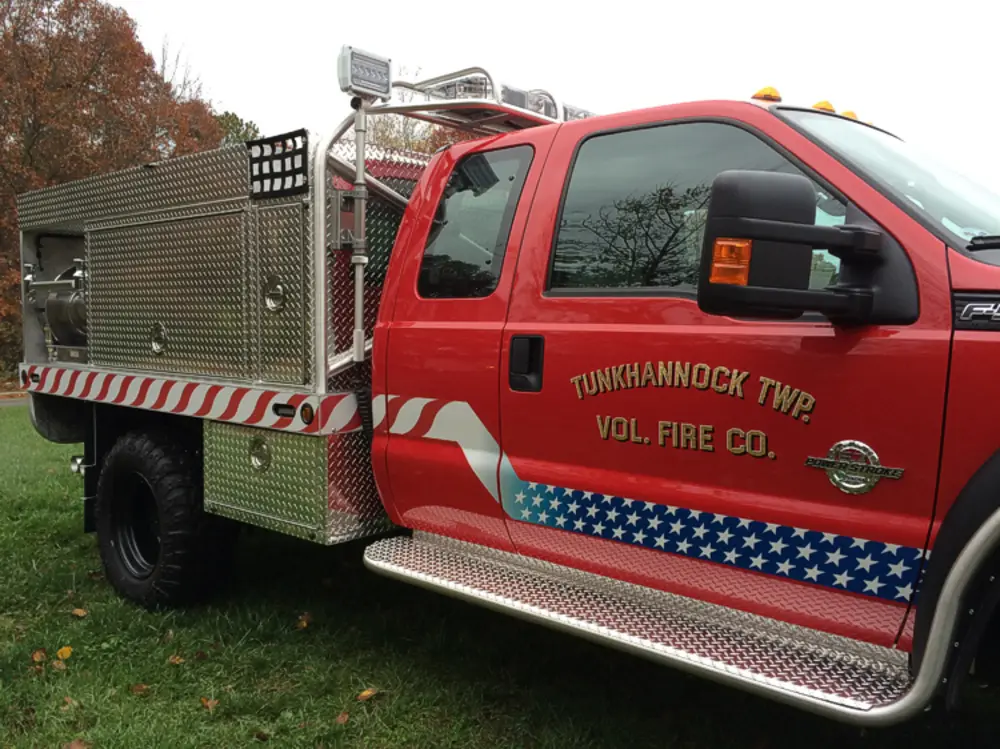 Exterior view of small fire truck showing cab, body compartments, and wheel/tire area.