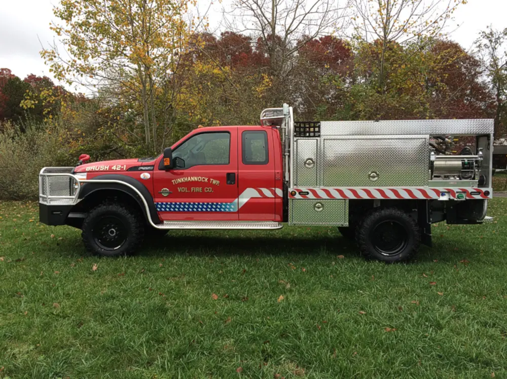 Exterior view of small fire truck showing cab, body compartments, and wheel/tire area.