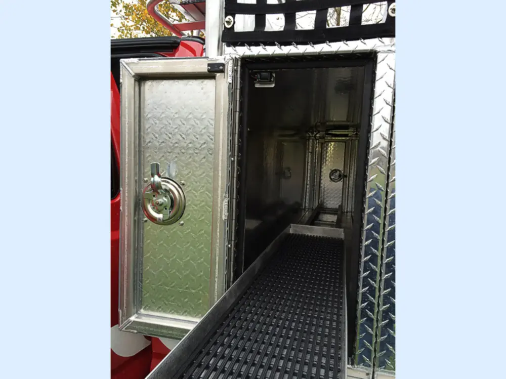 Exterior view of small fire truck showing cab, body compartments, and wheel/tire area.