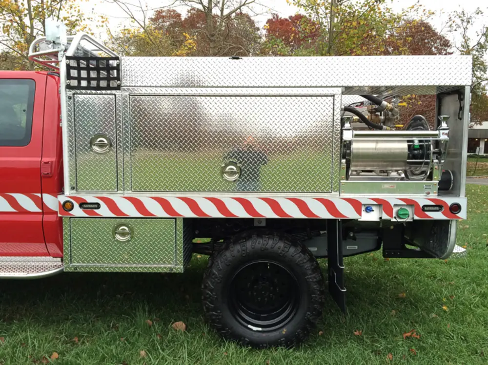 Exterior view of small fire truck showing cab, body compartments, and wheel/tire area.