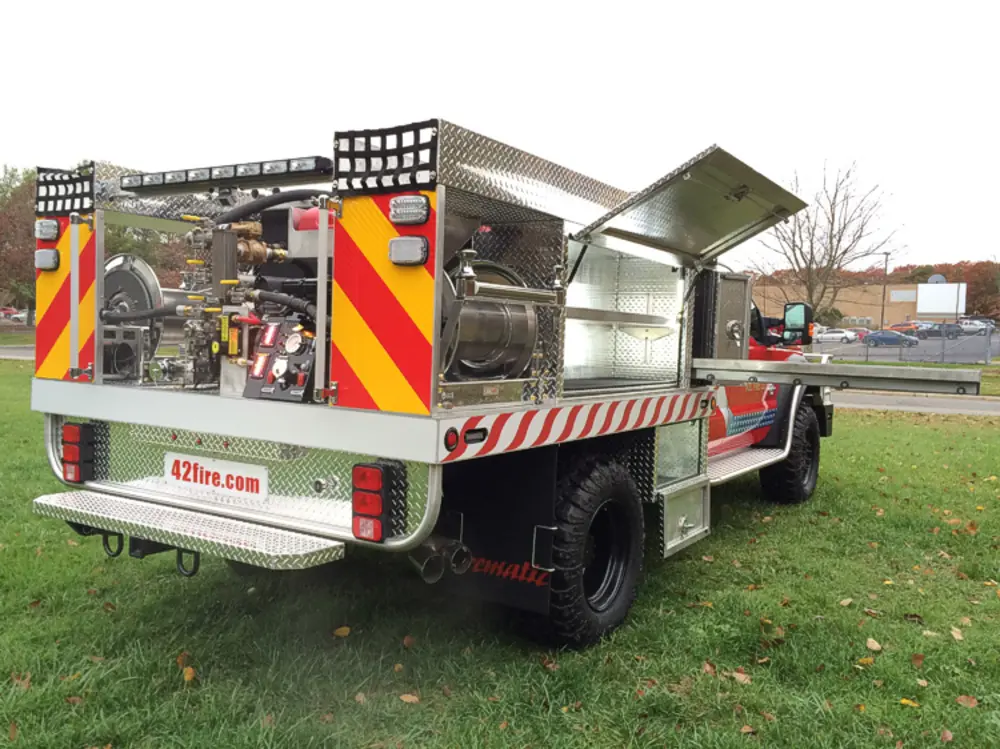 Exterior view of small fire truck showing cab, body compartments, and wheel/tire area.