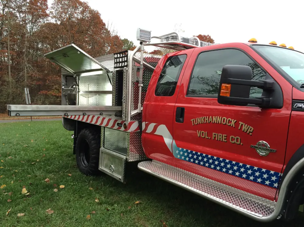 Exterior view of small fire truck showing cab, body compartments, and wheel/tire area.