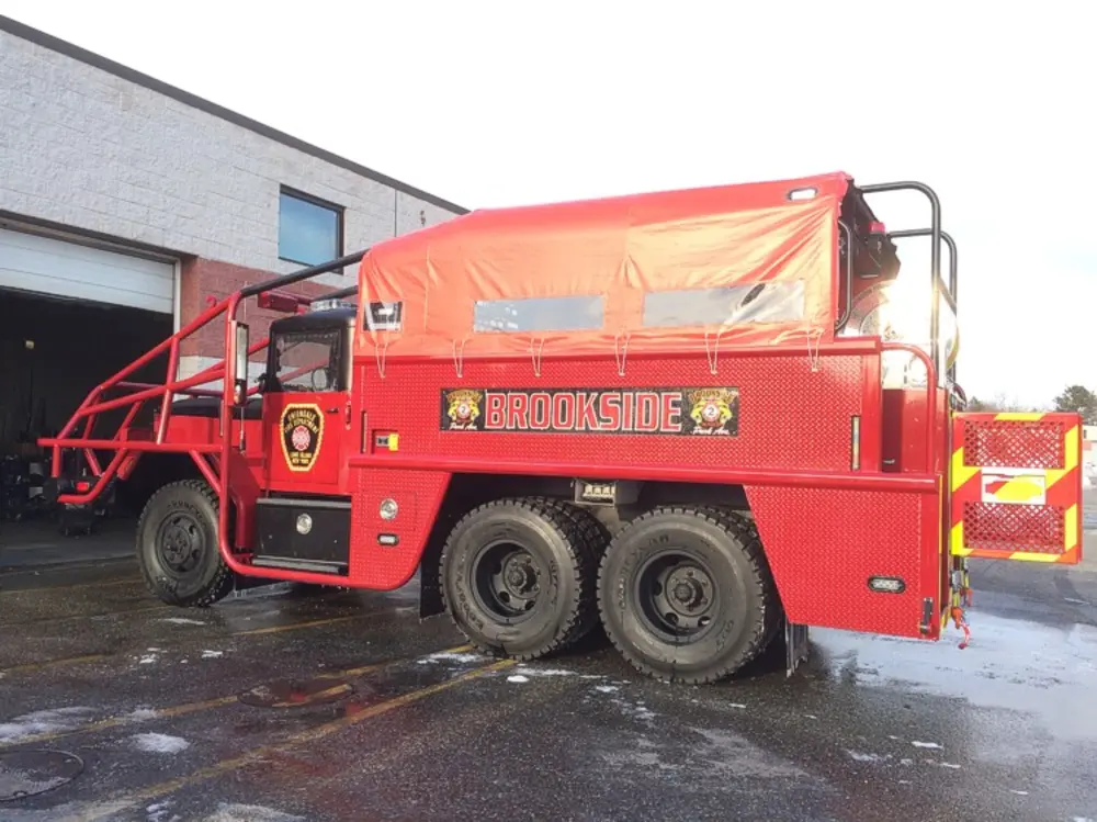 Exterior view of small fire truck showing cab, body compartments, and wheel/tire area.