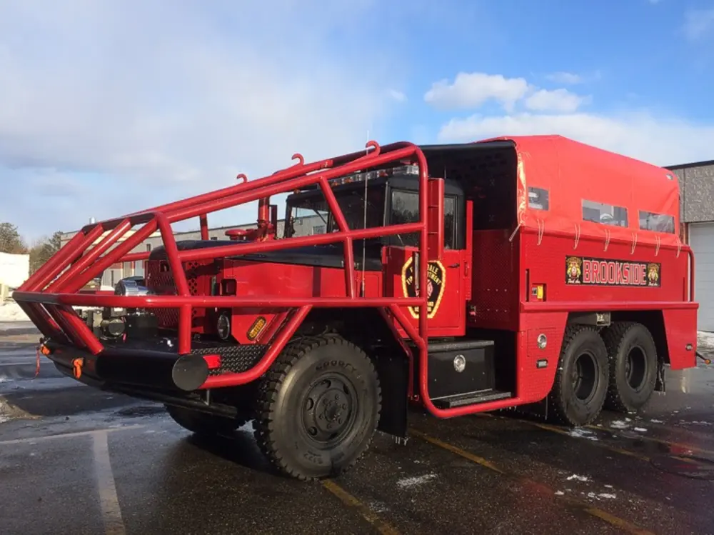 Exterior view of small fire truck showing cab, body compartments, and wheel/tire area.