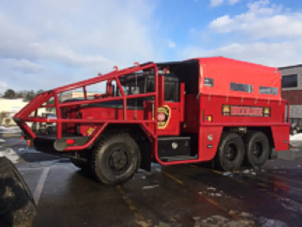 Exterior view of small fire truck showing cab, body compartments, and wheel/tire area.