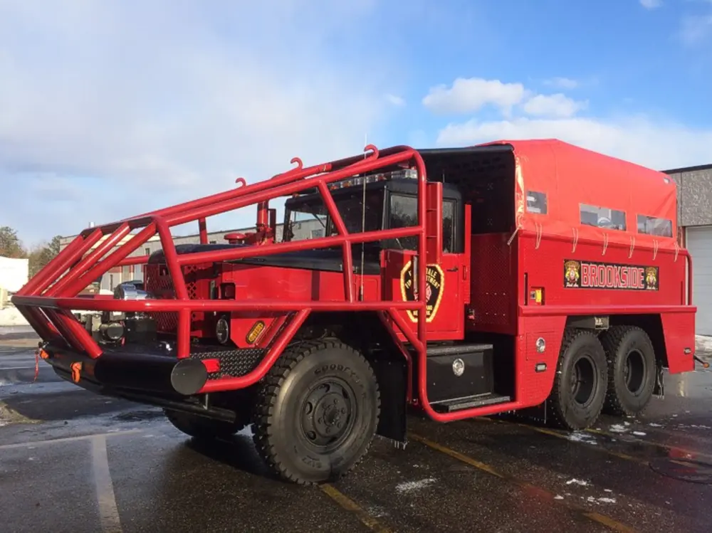 Exterior view of small fire truck showing cab, body compartments, and wheel/tire area.