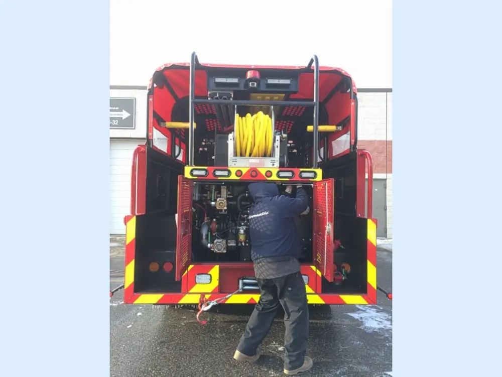 Exterior view of small fire truck showing cab, body compartments, and wheel/tire area.
