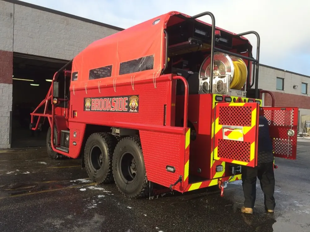 Exterior view of small fire truck showing cab, body compartments, and wheel/tire area.