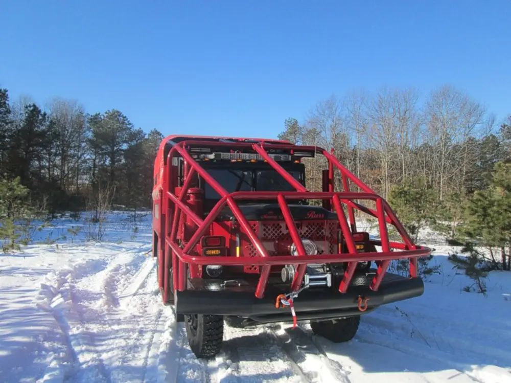 Exterior view of small fire truck showing cab, body compartments, and wheel/tire area.