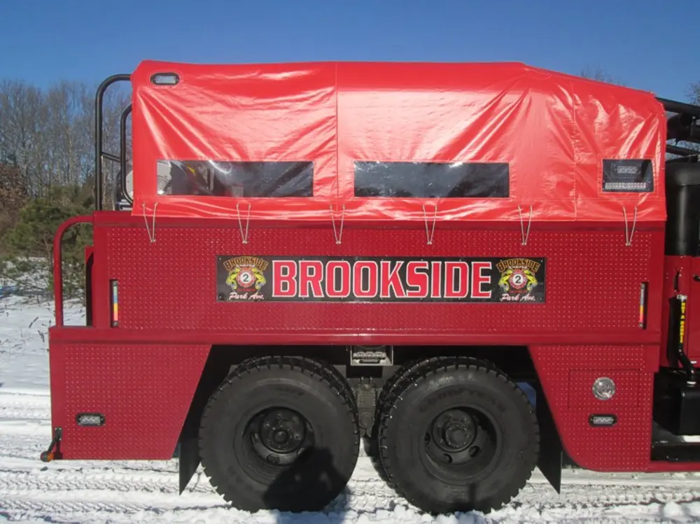 Exterior view of small fire truck showing cab, body compartments, and wheel/tire area.