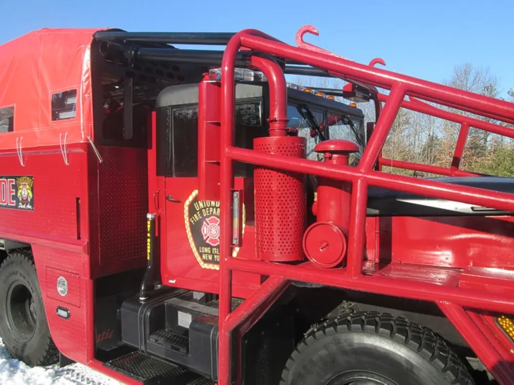 Exterior view of small fire truck showing cab, body compartments, and wheel/tire area.