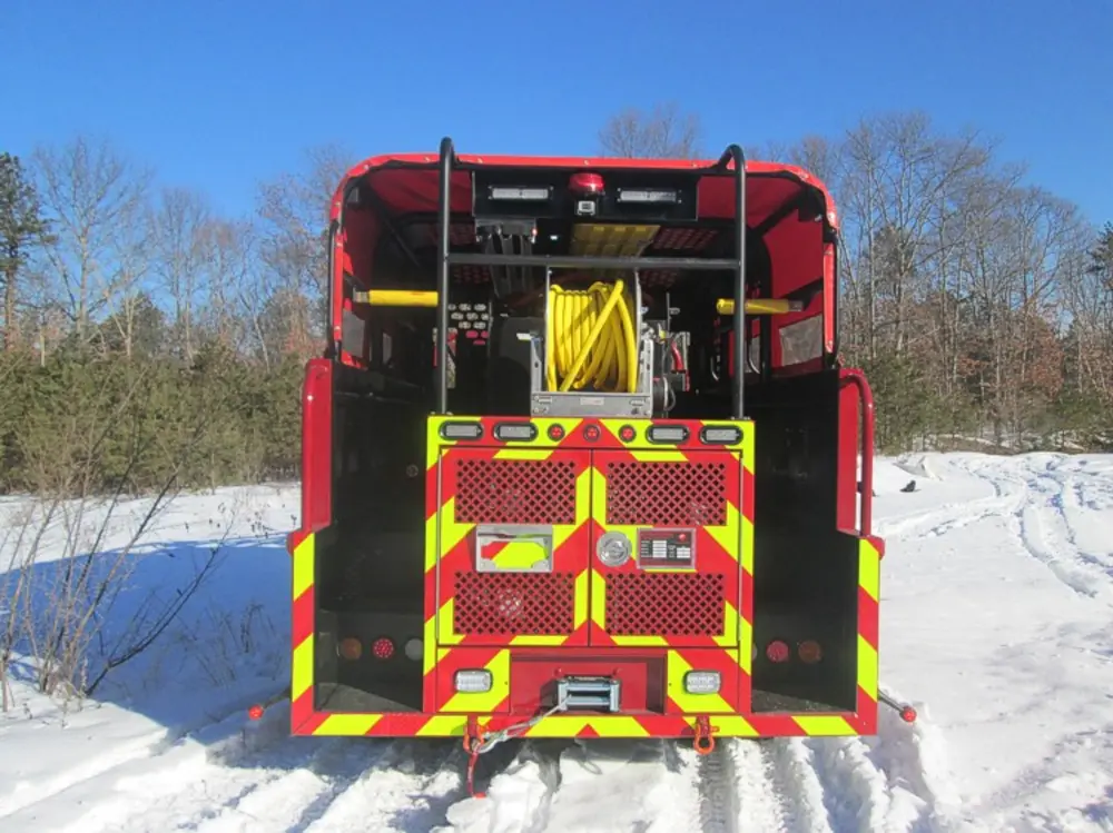 Exterior view of small fire truck showing cab, body compartments, and wheel/tire area.