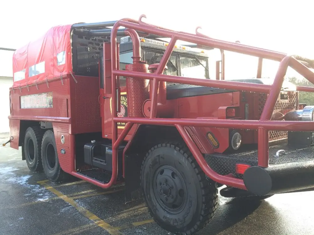 Exterior view of small fire truck showing cab, body compartments, and wheel/tire area.