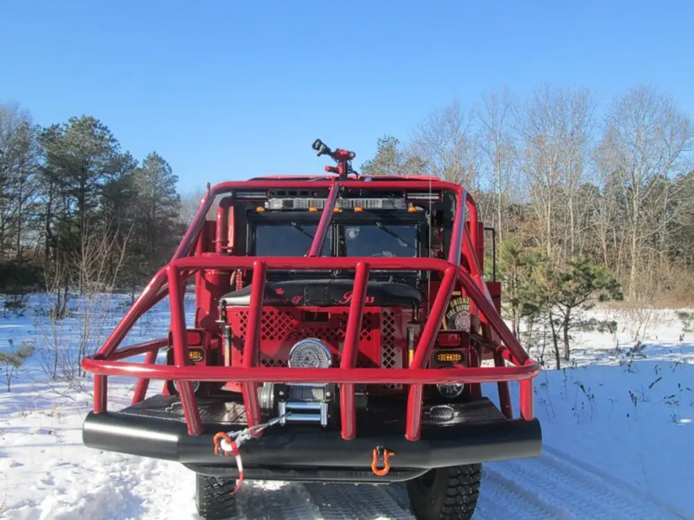 Exterior view of small fire truck showing cab, body compartments, and wheel/tire area.