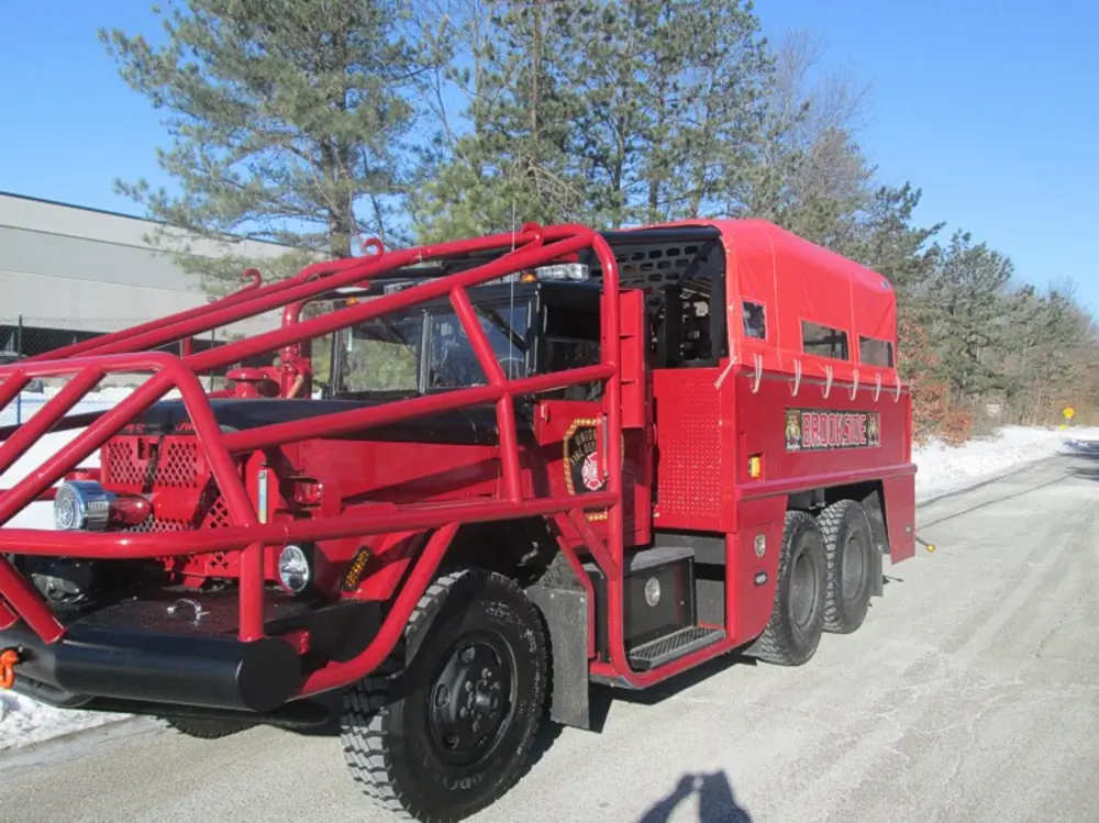 Exterior view of small fire truck showing cab, body compartments, and wheel/tire area.